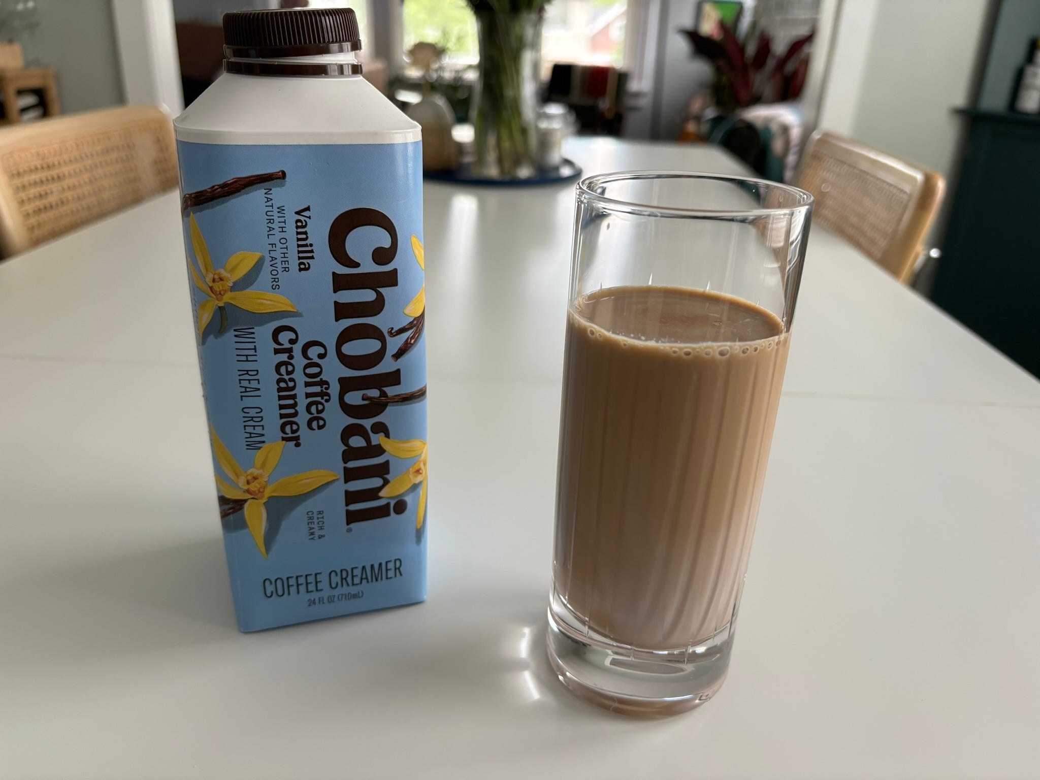 Chobani vanilla coffee creamer next to light-colored glass of coffee