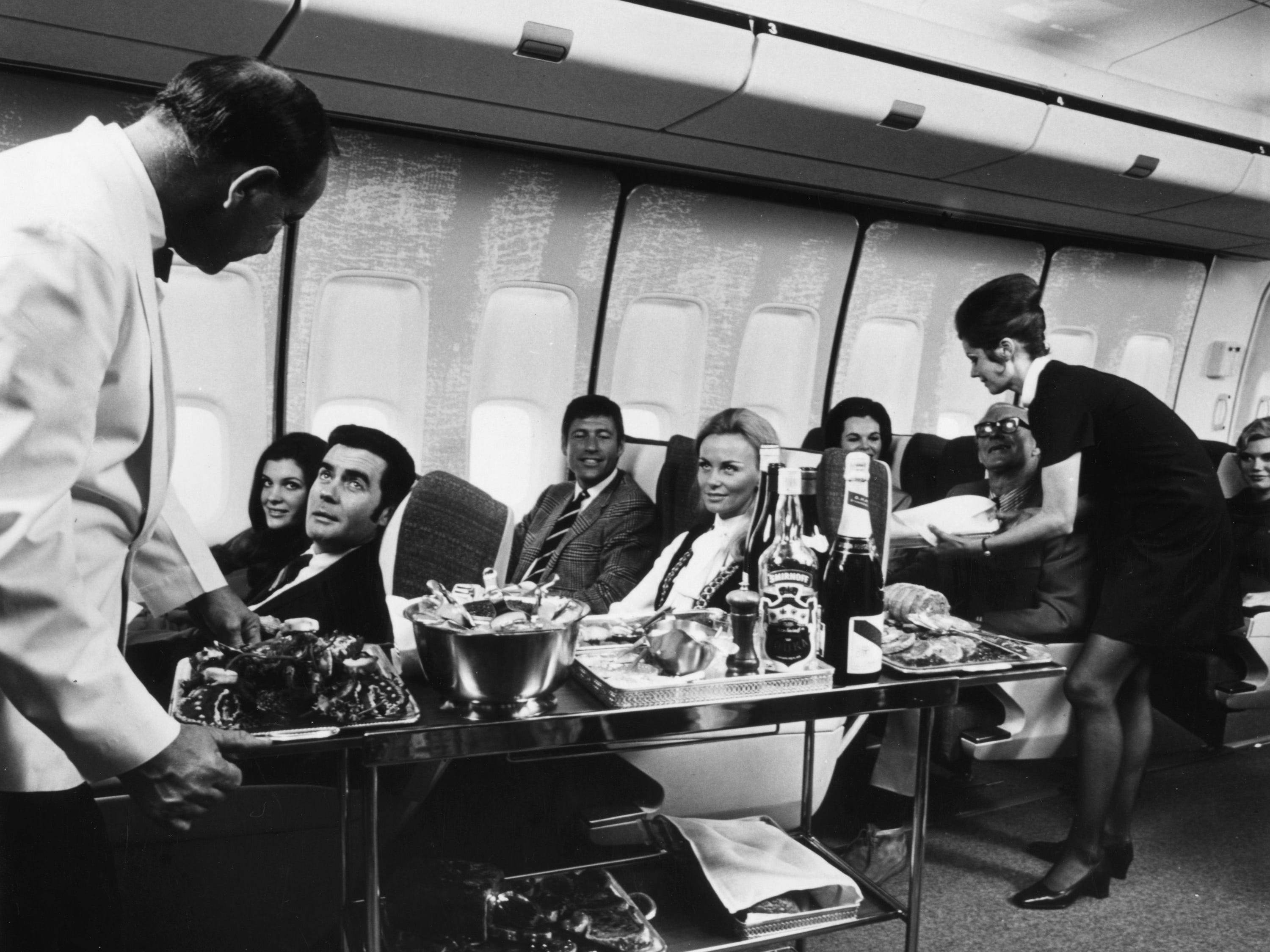 A steward and stewardess serving first-class passengers with drinks and refreshments on board a Boeing 747.