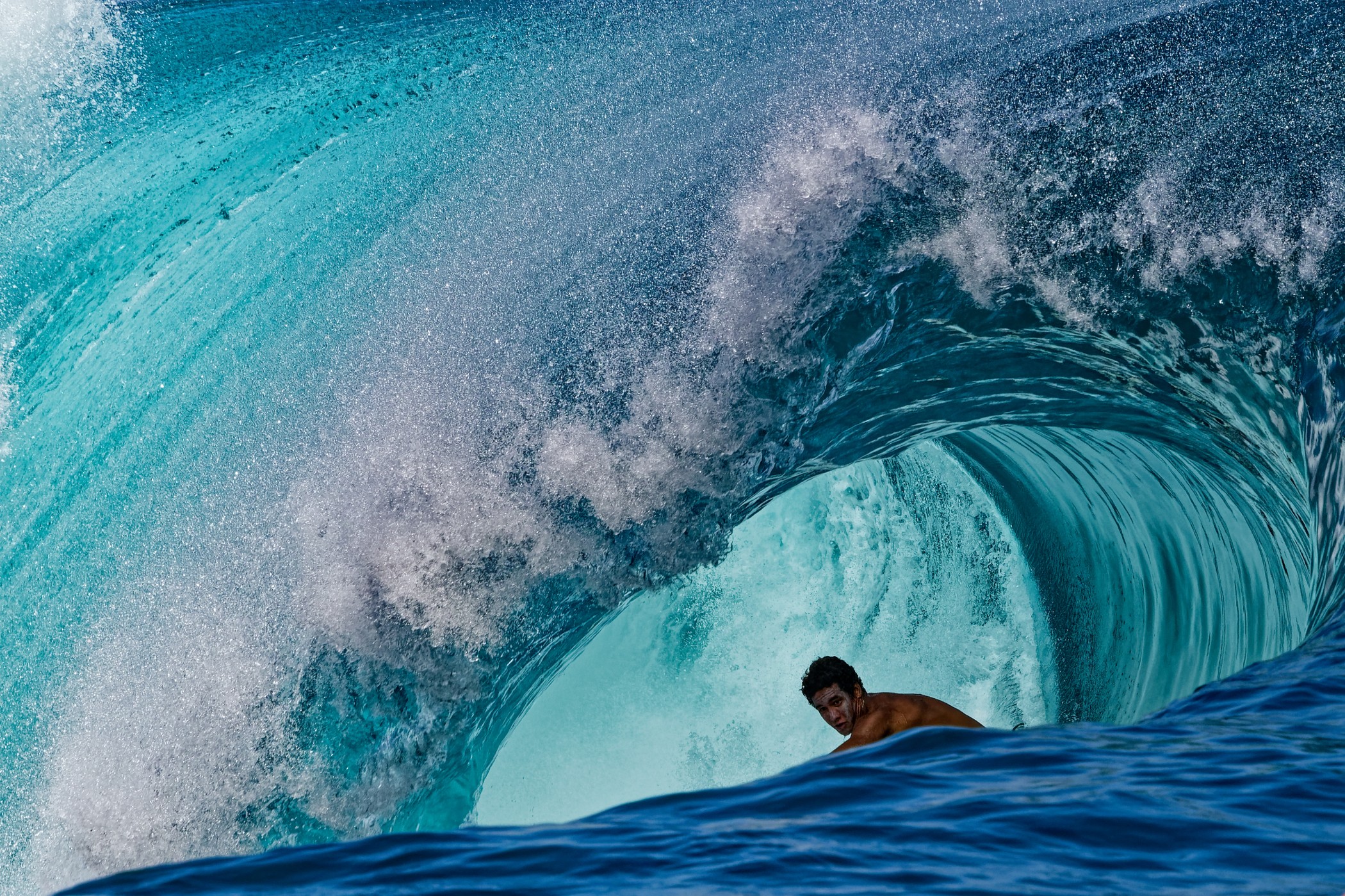 A surfer, seen inside a large curl of a wave.
