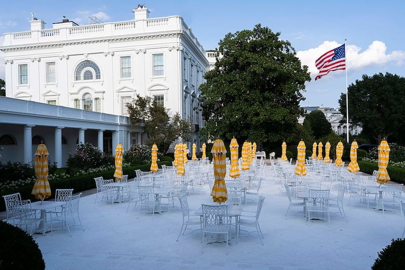Metal tables and chairs along with yellow umbrellas decorate a paved over historic White House Rose Garden lawn.