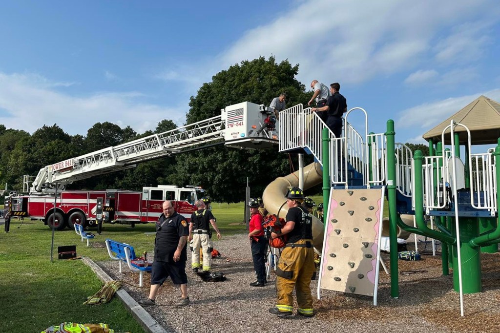 Firefighters using a ladder truck to rescue someone from a playground slide.