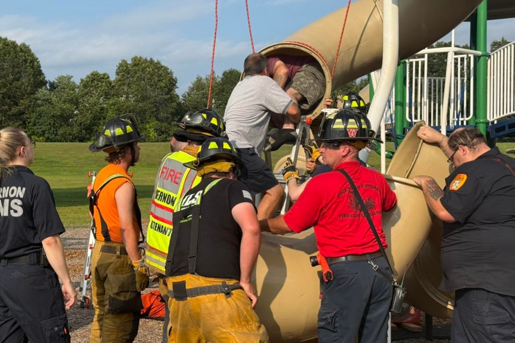 Firefighters rescuing a person stuck in a playground slide.