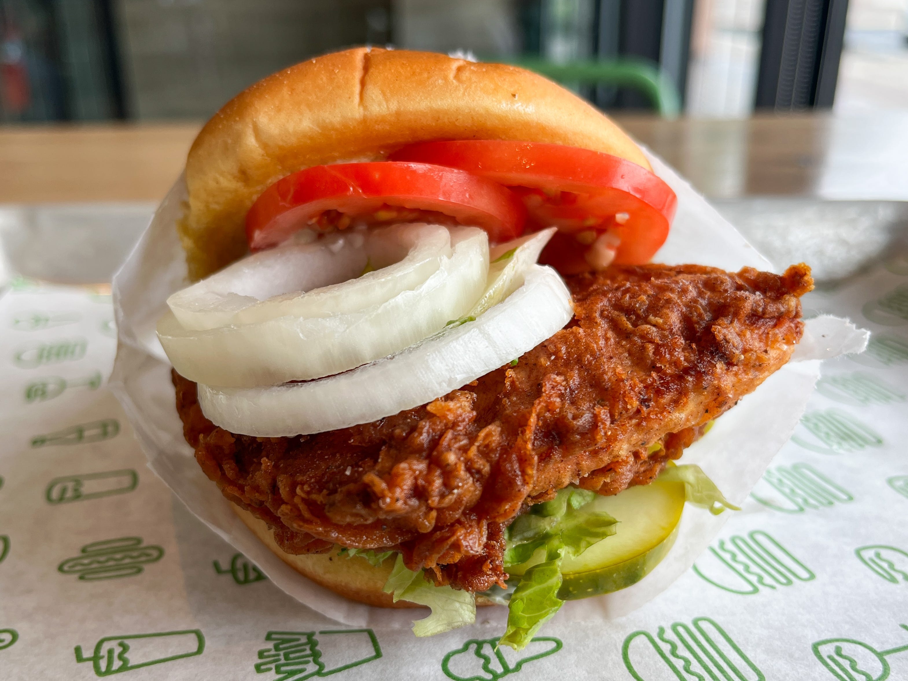 A fried-chicken sandwich with pickles, lettuce, tomatoes, and onions.