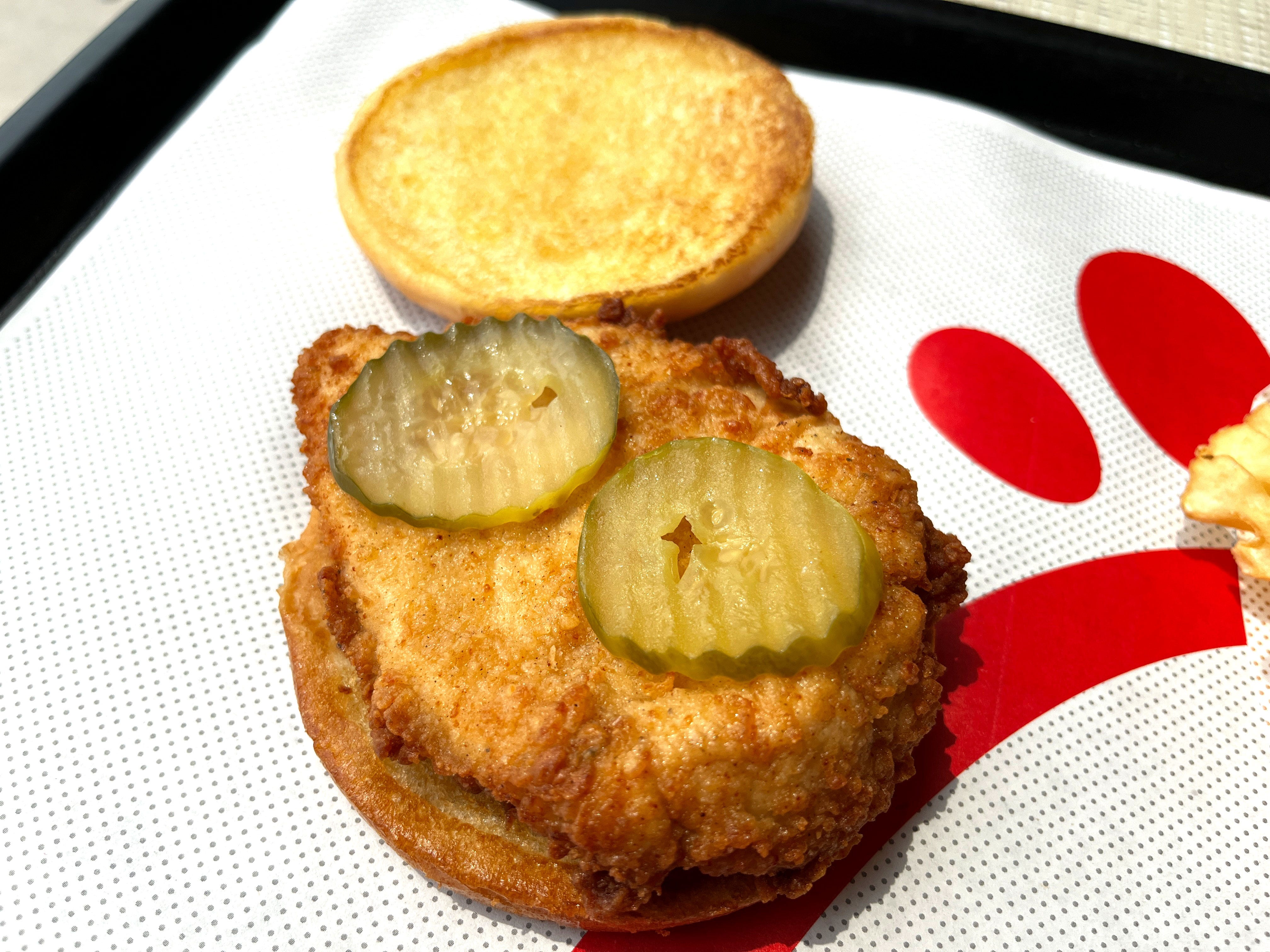 An open fried-chicken sandwich topped with two pickle chips on a tray at Chick-fil-A.