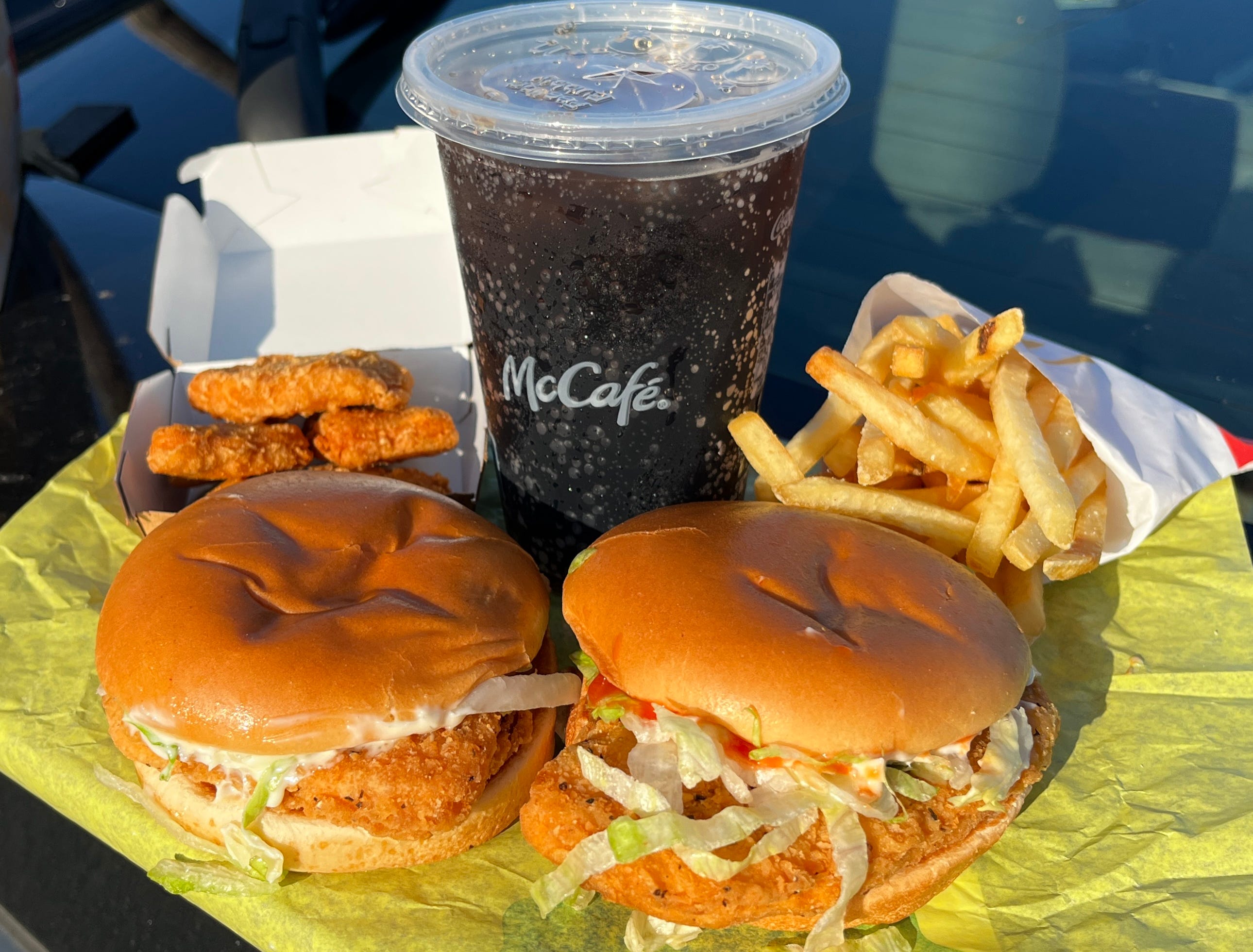 Two fried-chicken sandwiches, fries, nuggets, and a drink from McDonald's on yellow paper.