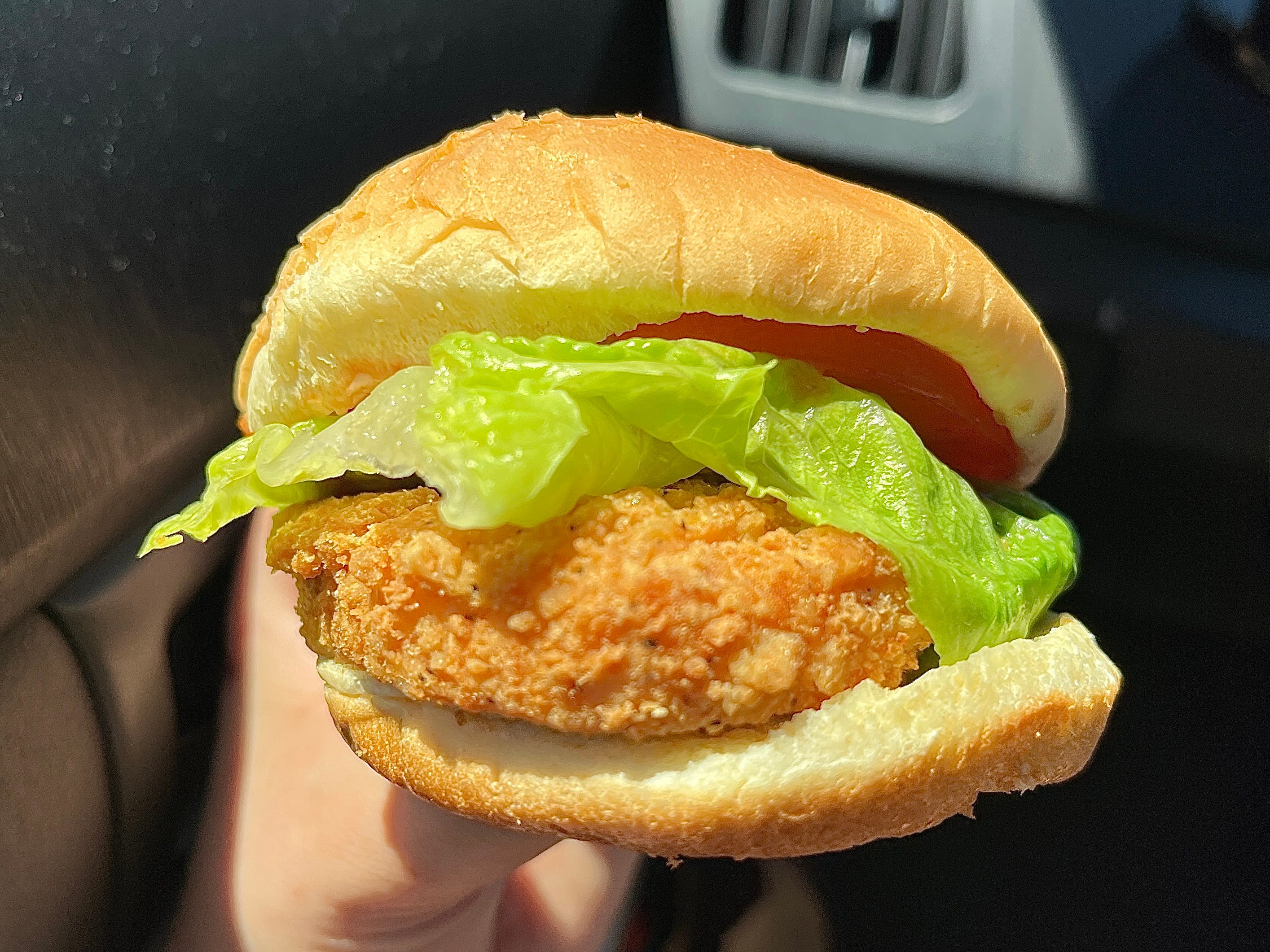 A hand holding a fried-chicken sandwich with lettuce and tomato.
