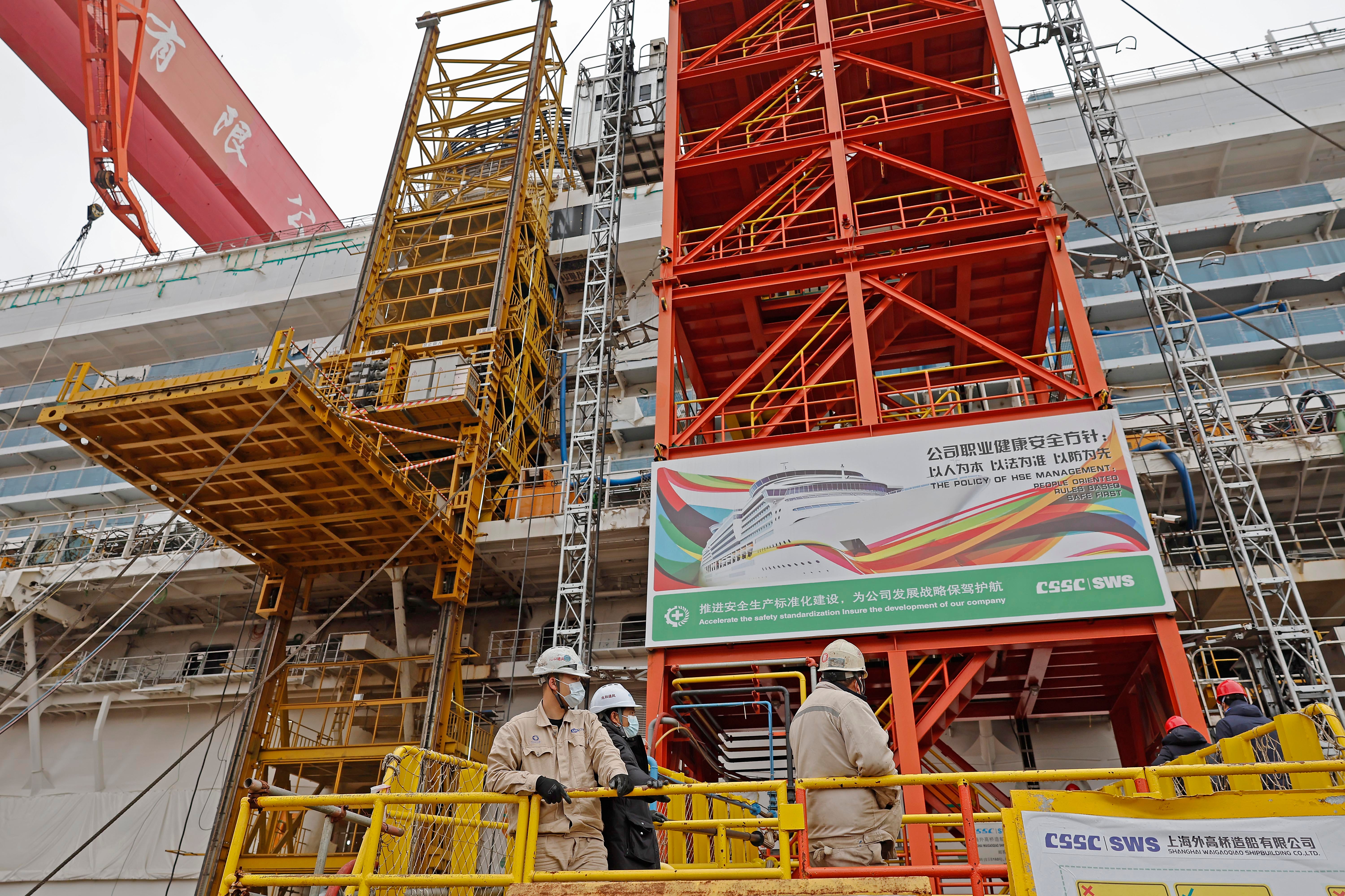 Chinese works stand in front of a large cruise ship being built at a Chinese shipyard.
