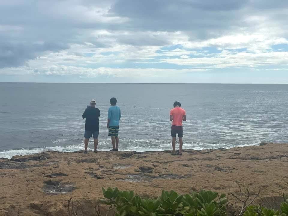 Two boys stand by the water alongside their dad.