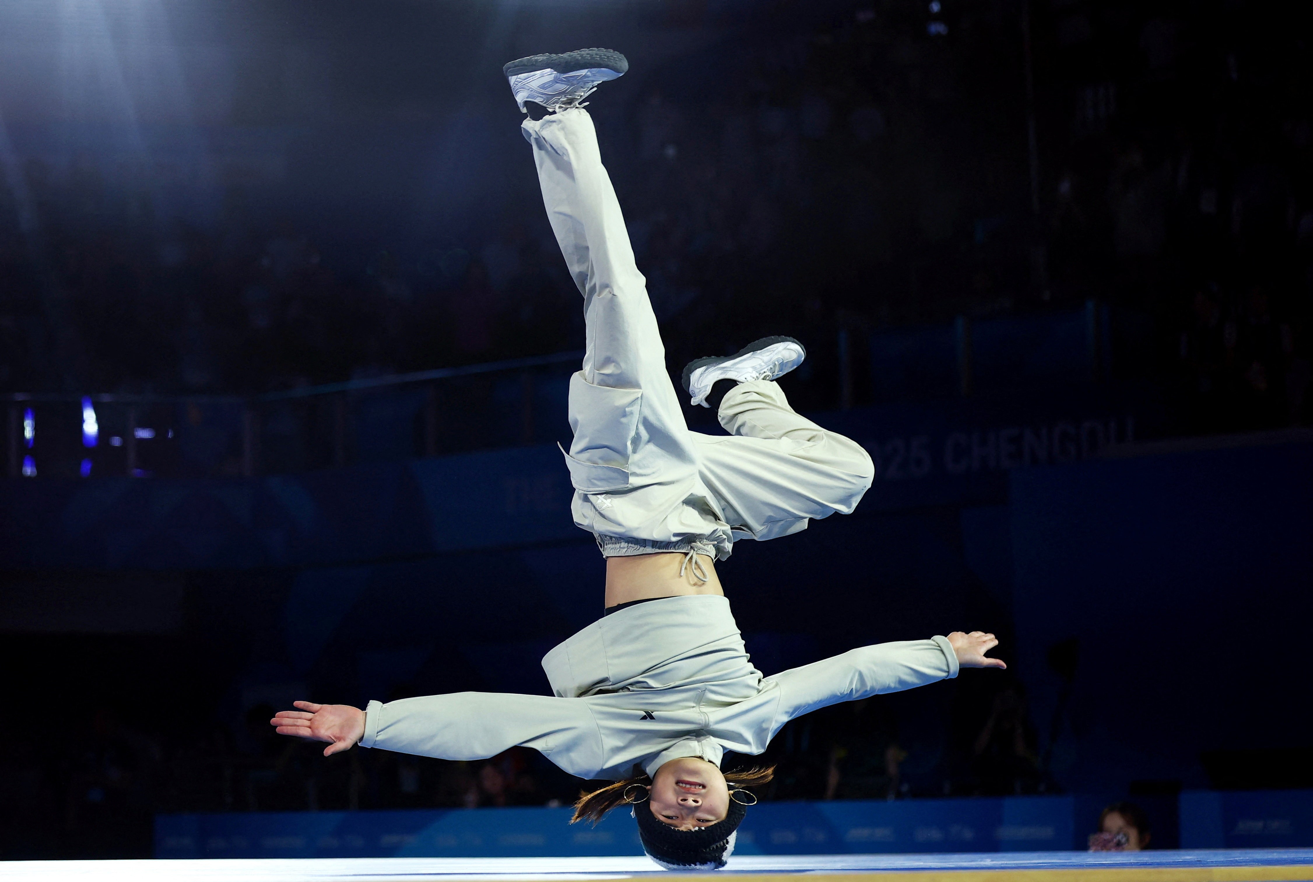 A breakdancing competitor spins on their head with arms outstretched.
