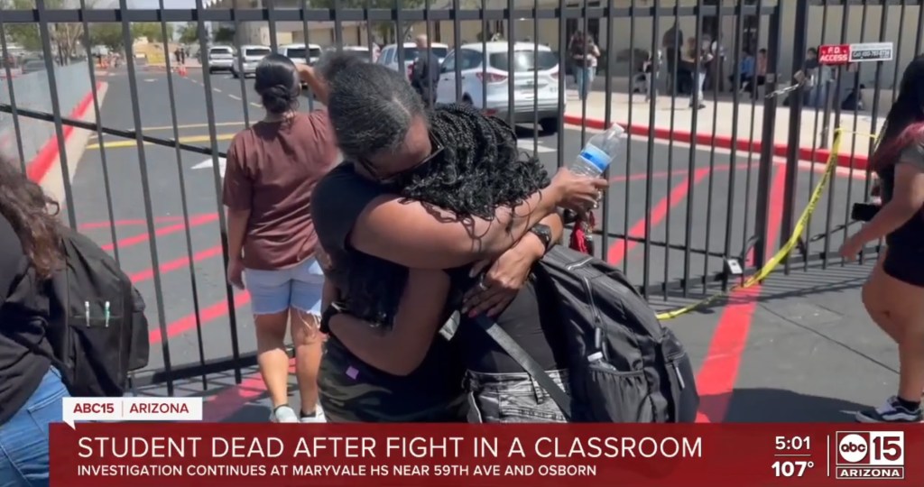 Two people hugging outside a school after a student died following a classroom fight.