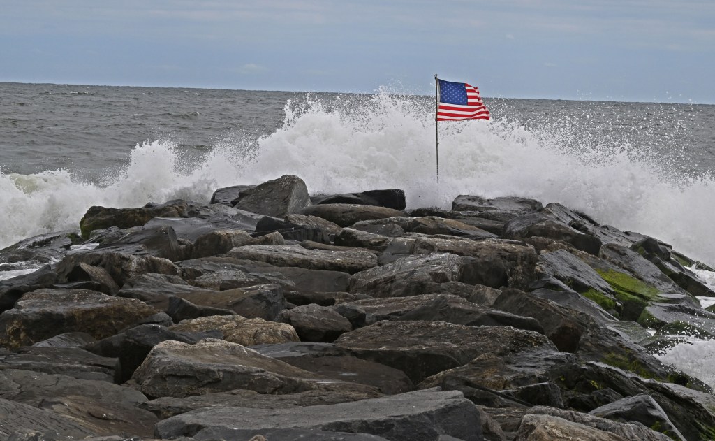 American flag on rocks amidst crashing waves.