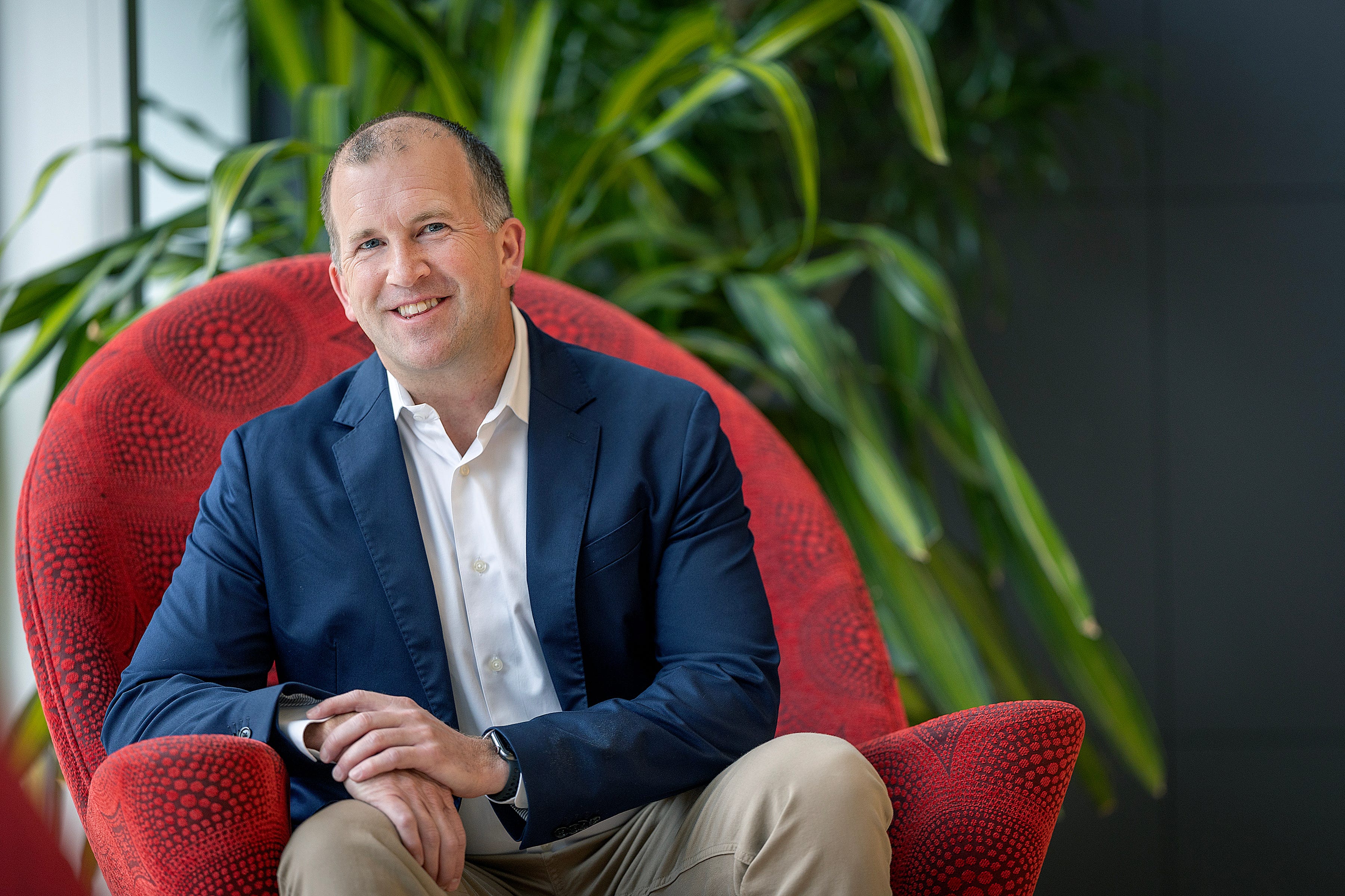 Michael Fiddelke sitting in a red chair in front of a plant looking at the camera