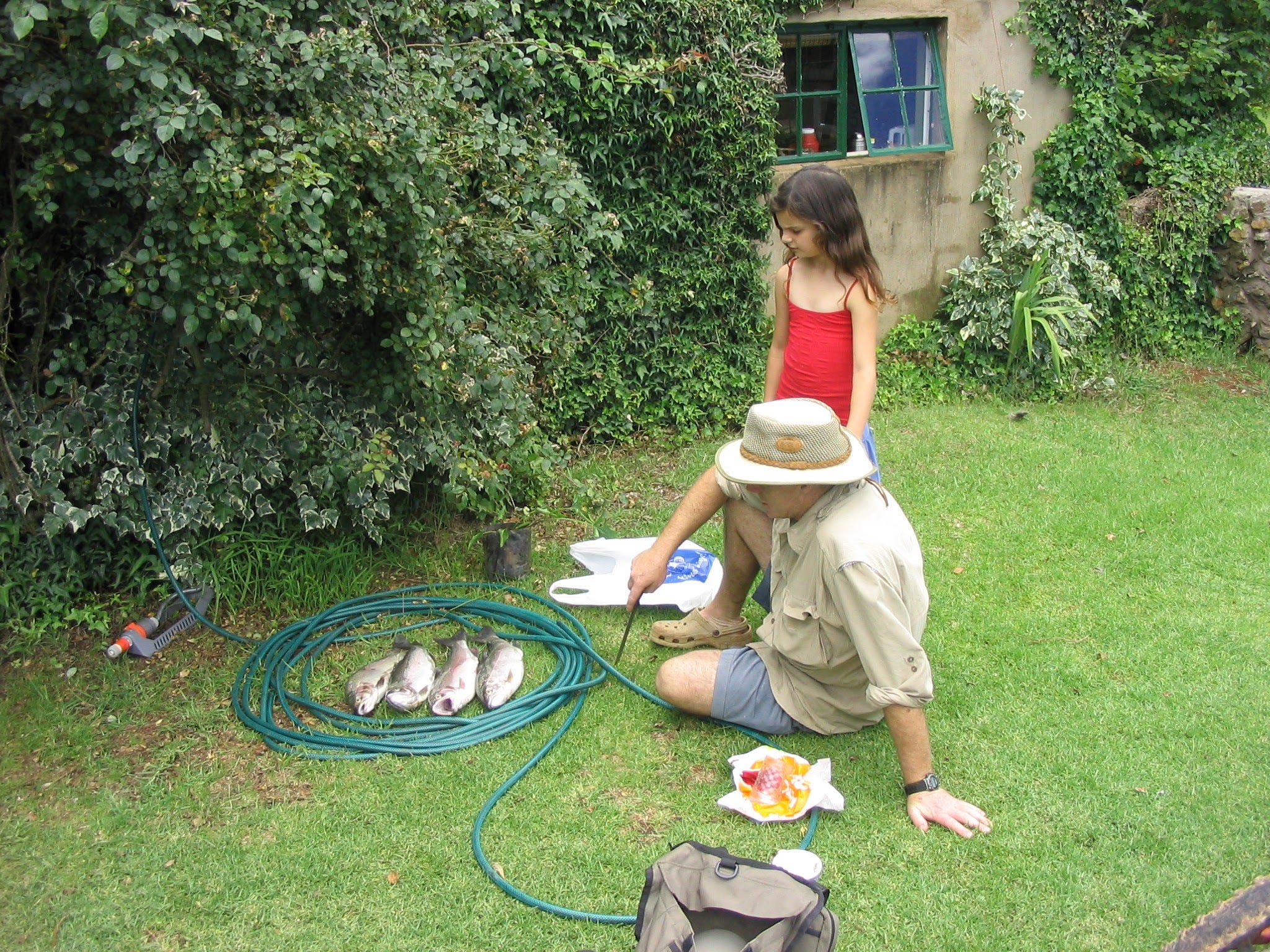 The author with her father on a lawn, looking at a few fish inside a circled up hose.
