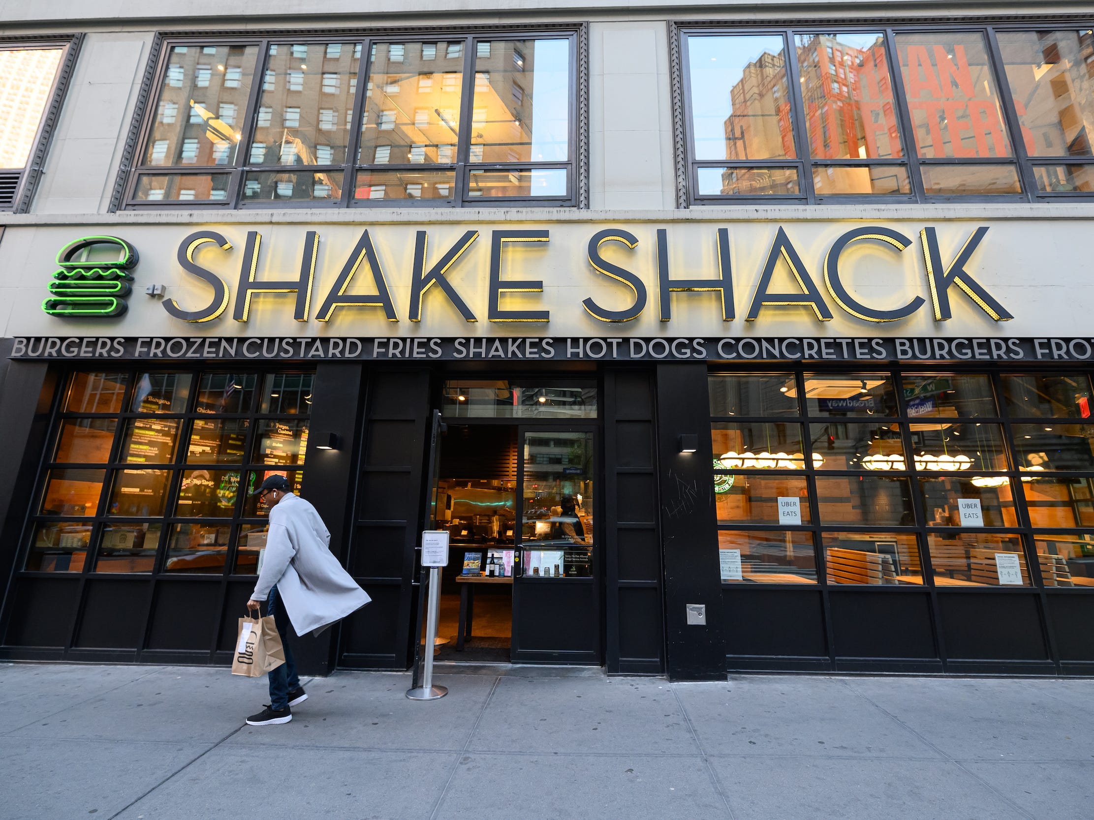 A person walking on the sidewalk outside a Shake Shack.