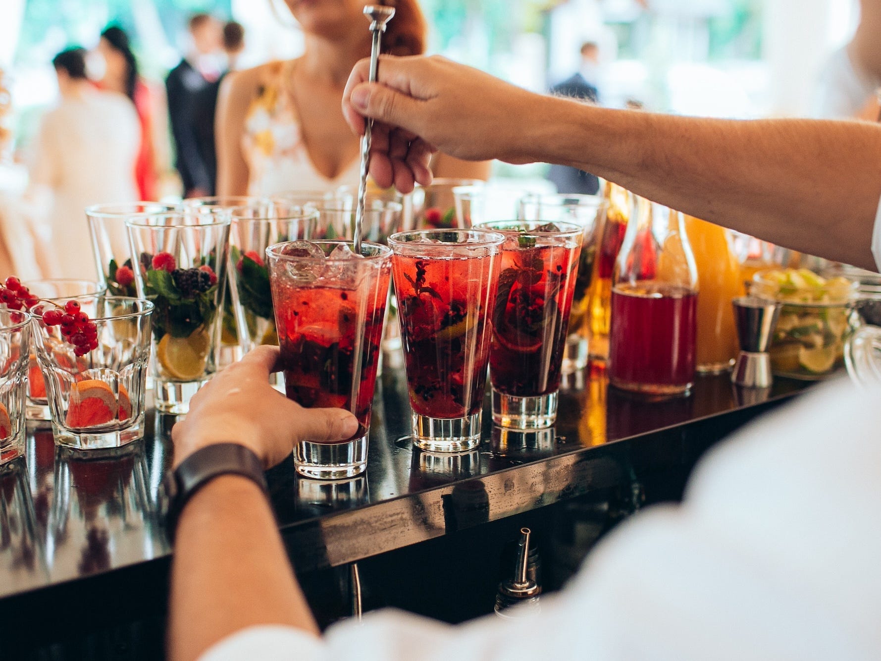 A bartender mixes pink cocktails at a full bar.