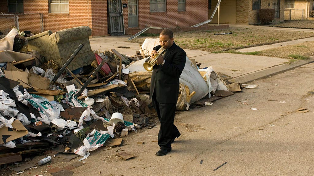 A man plays the trumpet among debris after Hurricane Katrina.