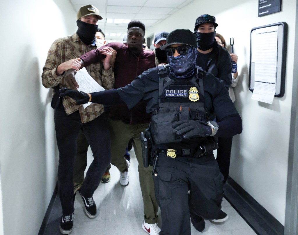 Federal agents detaining a man in a hallway.