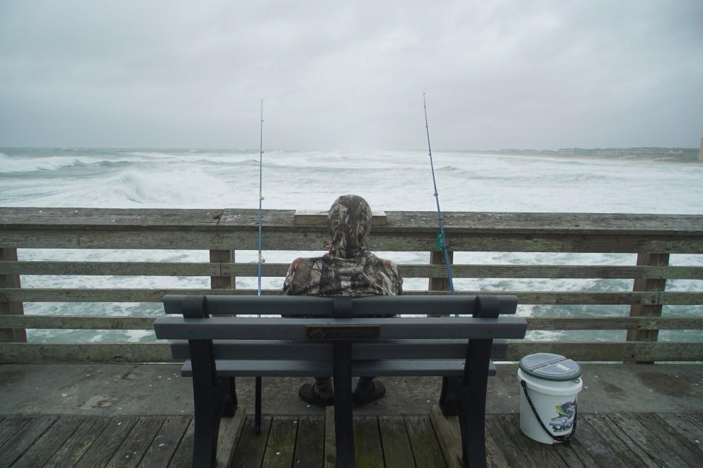 Sebastian Kettner fishes on Jennette's Pier as waves from Hurricane Erin crash ashore in Nags Head, N.C., Thursday, Aug. 21, 2025.