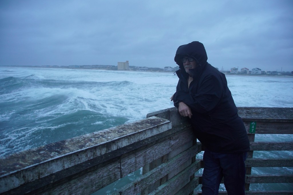 A man smokes a cigarette at the end of Jennette's Pier as waves from Hurricane Erin crash ashore in Nags Head, N.C., on Thursday, Aug. 21, 2025.