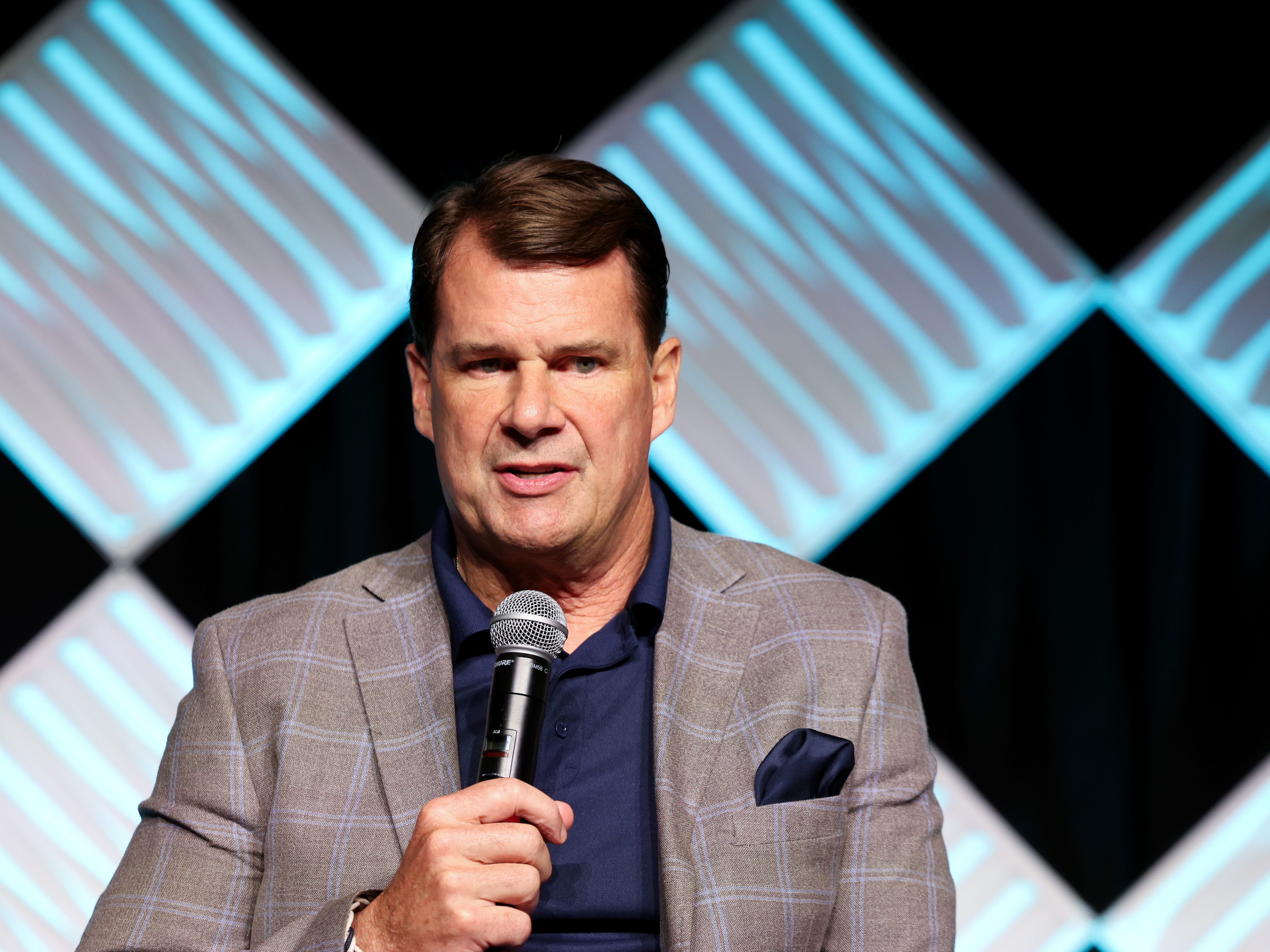Jim Farley, the CEO of Ford, is seen holding a microphone and speaking.
