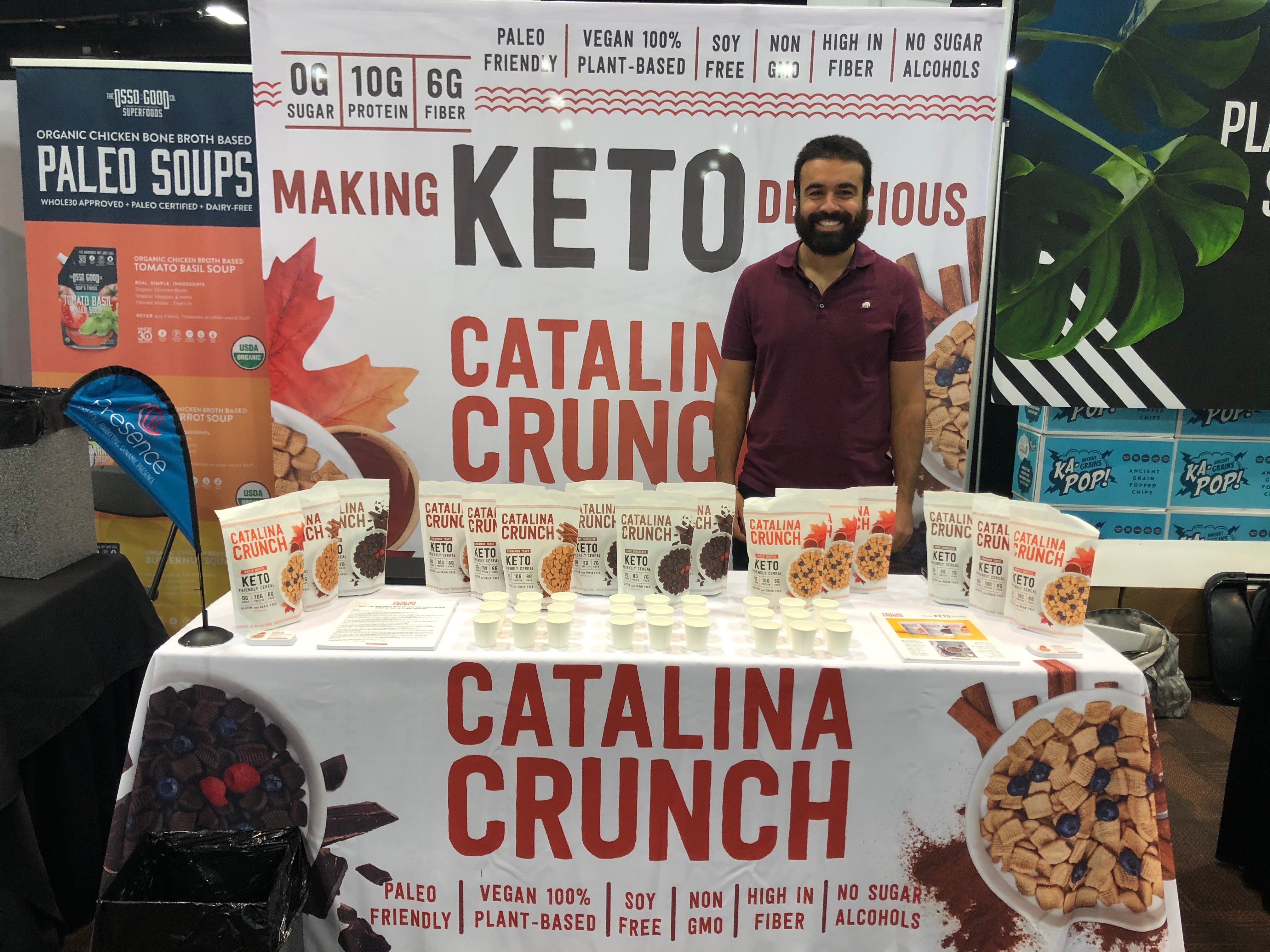 Krishna Kaliannan smiles as he stands at the Catalina Crunch booth at a trade show