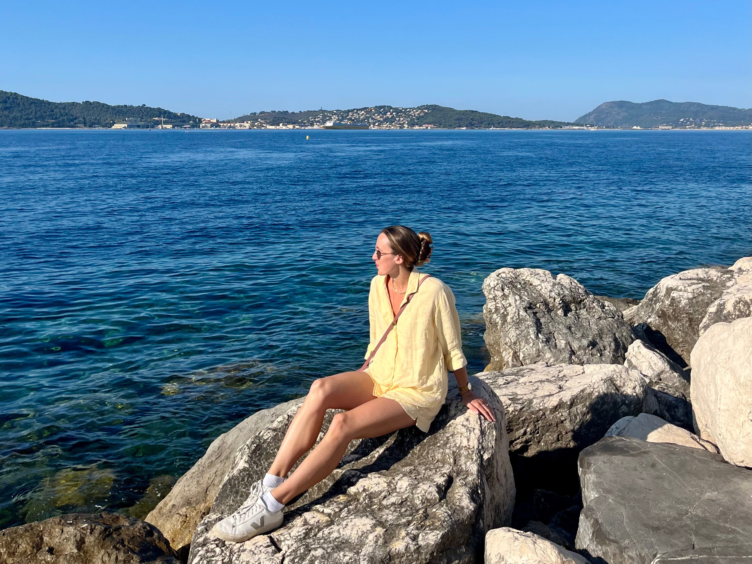 woman in yellow shirt sitting on rocks looking out to sea