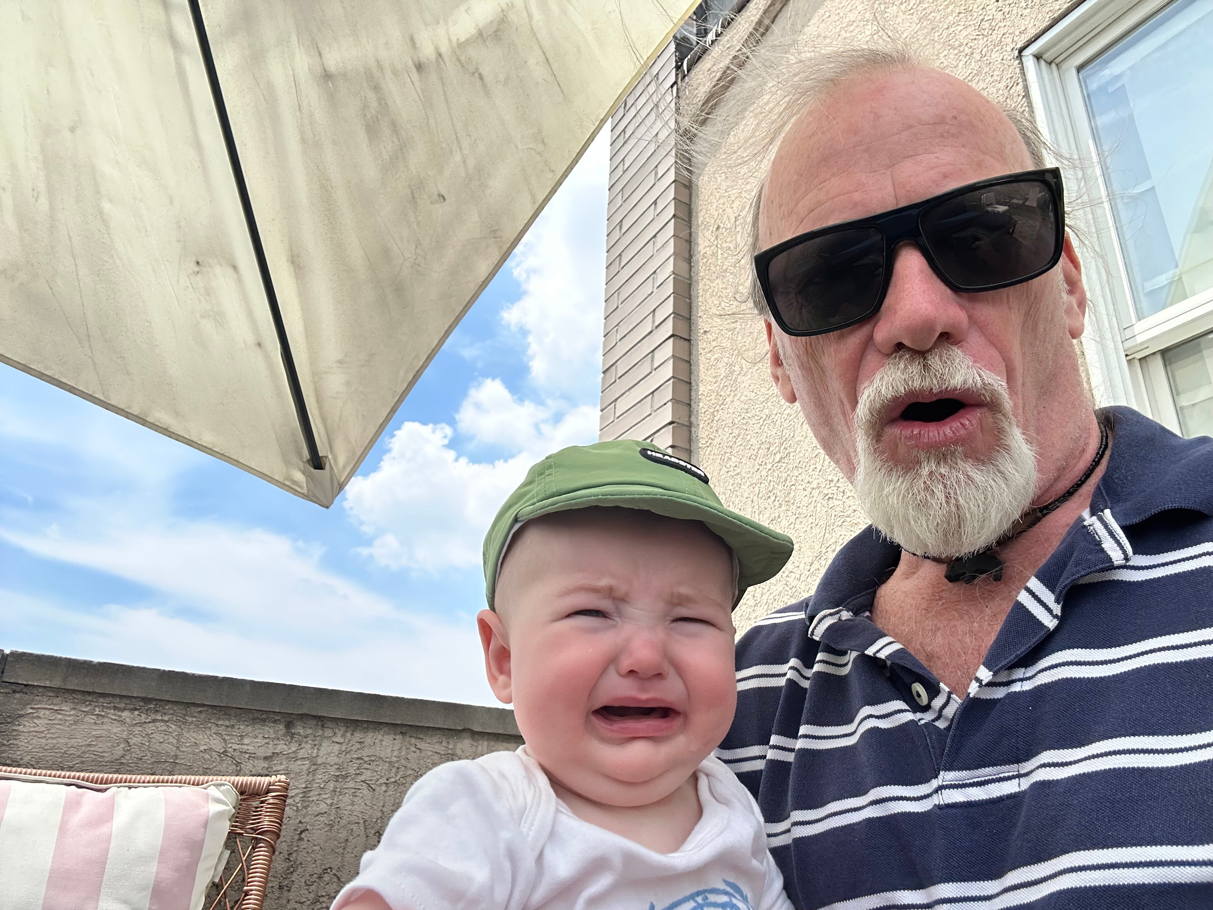 Steve makes a surprised face while his grandson cries on his lap.