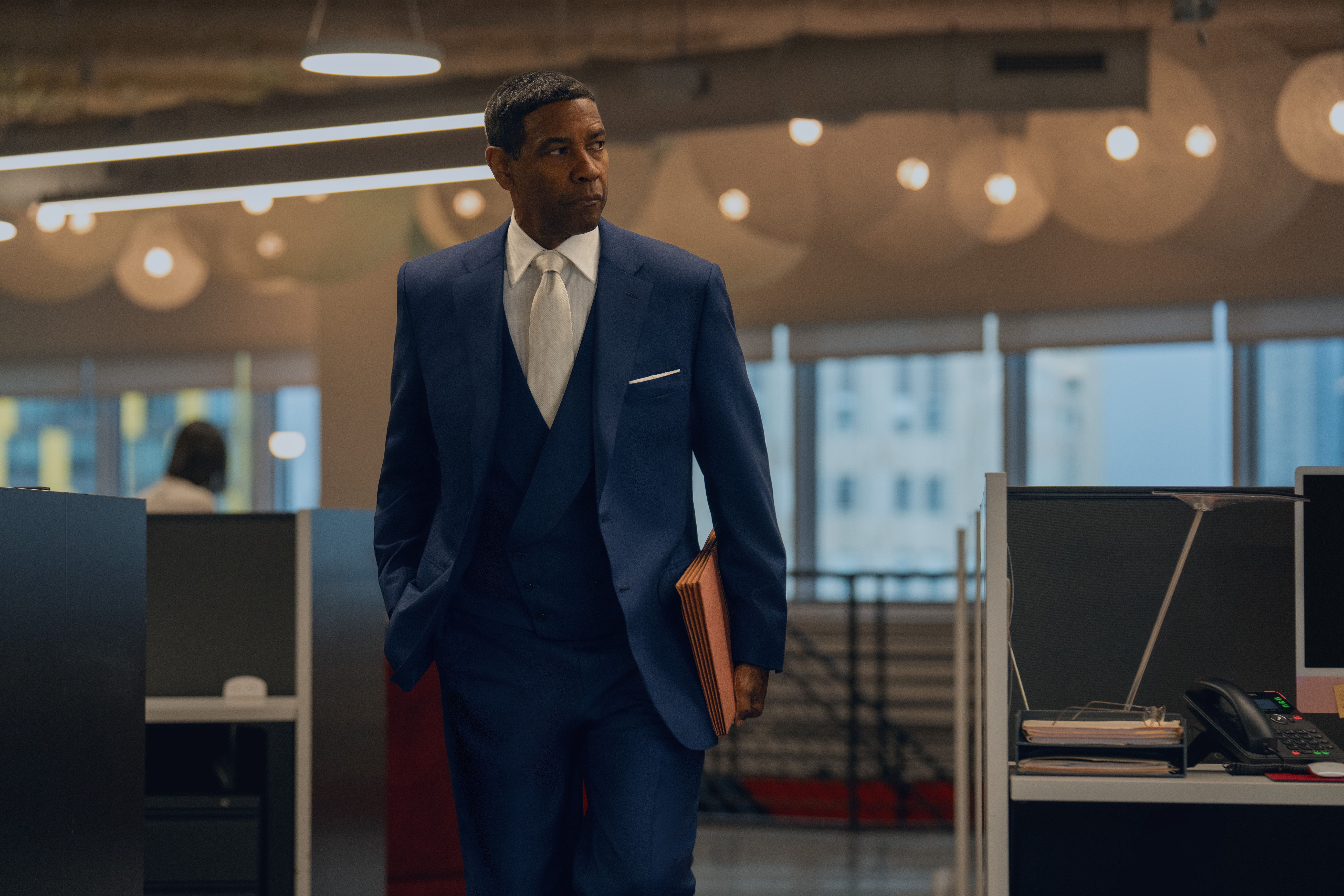 Denzel Washington in a blue suit holding a folder