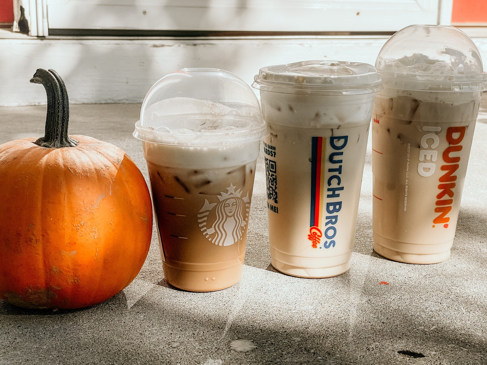 pumpkin next to pumpkin coffees from Starbucks, dutch bros, and dunkin'