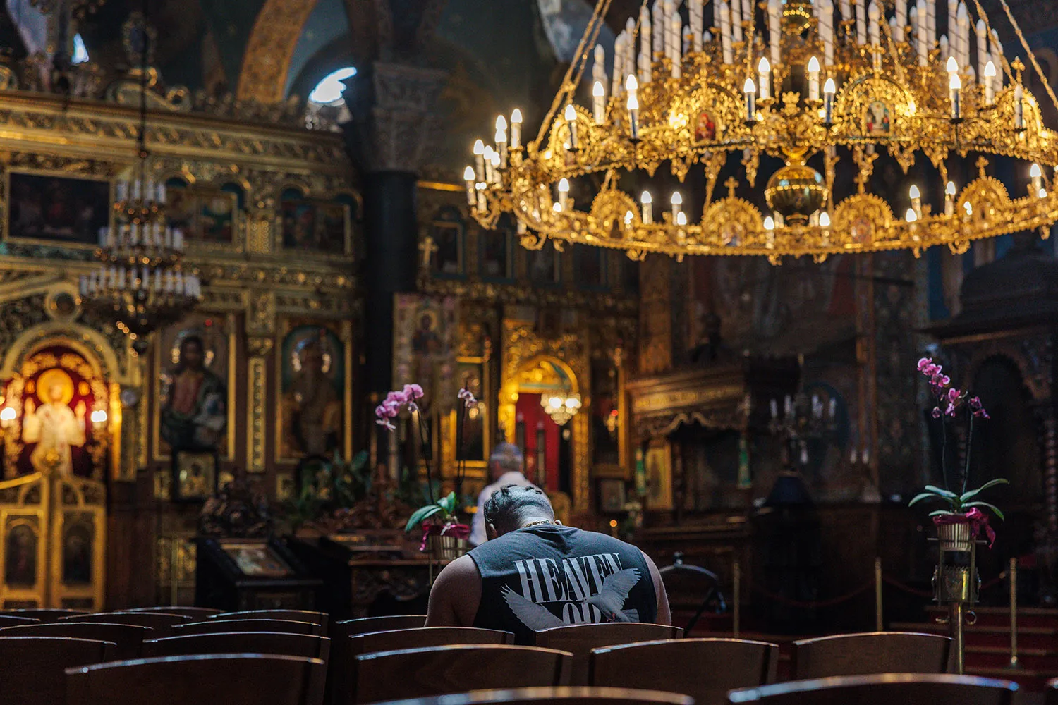 A man sits in a pfew of a church under an ornate chandelier.