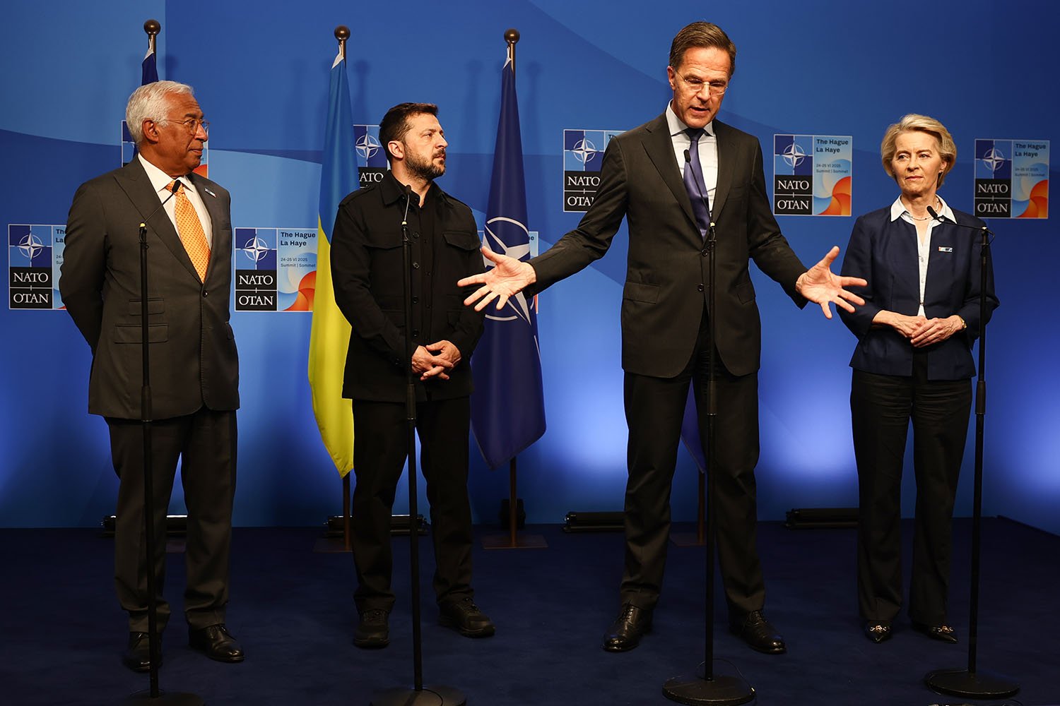 Four people stand on stage. Rutte gestures with his hands wide at his side as he talks.