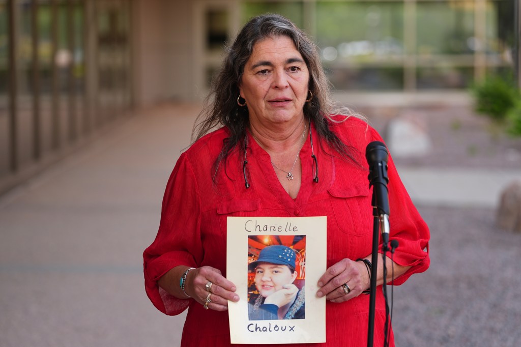 Woman in red shirt holding photo of Chanelle Chaloux at a press conference.