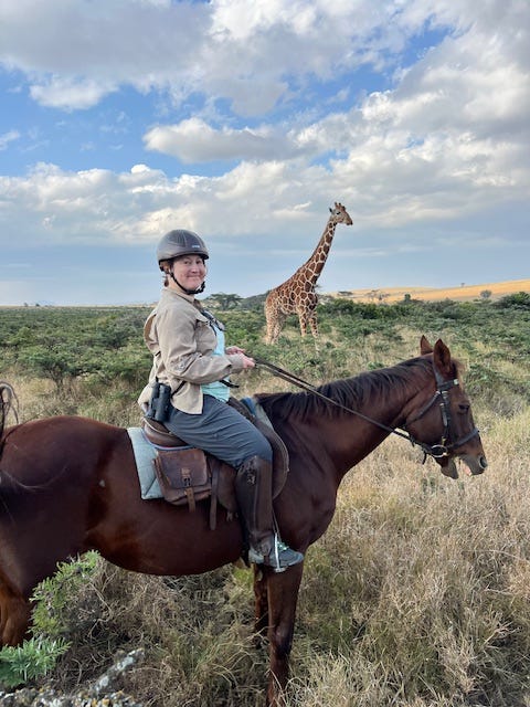 woman on horse with a giraffe in the background