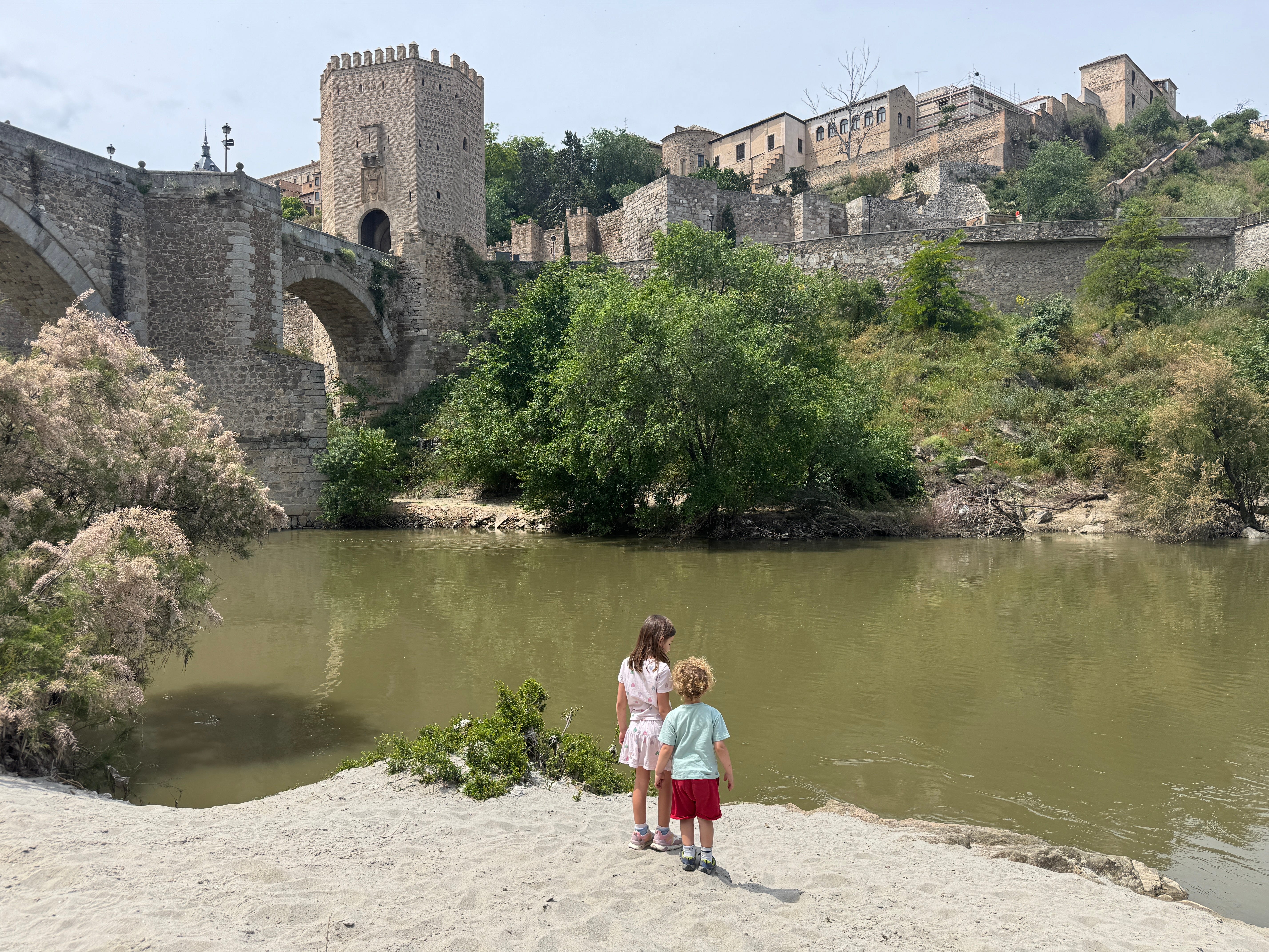 two young children standing on beach in front of spanish city with old style castle