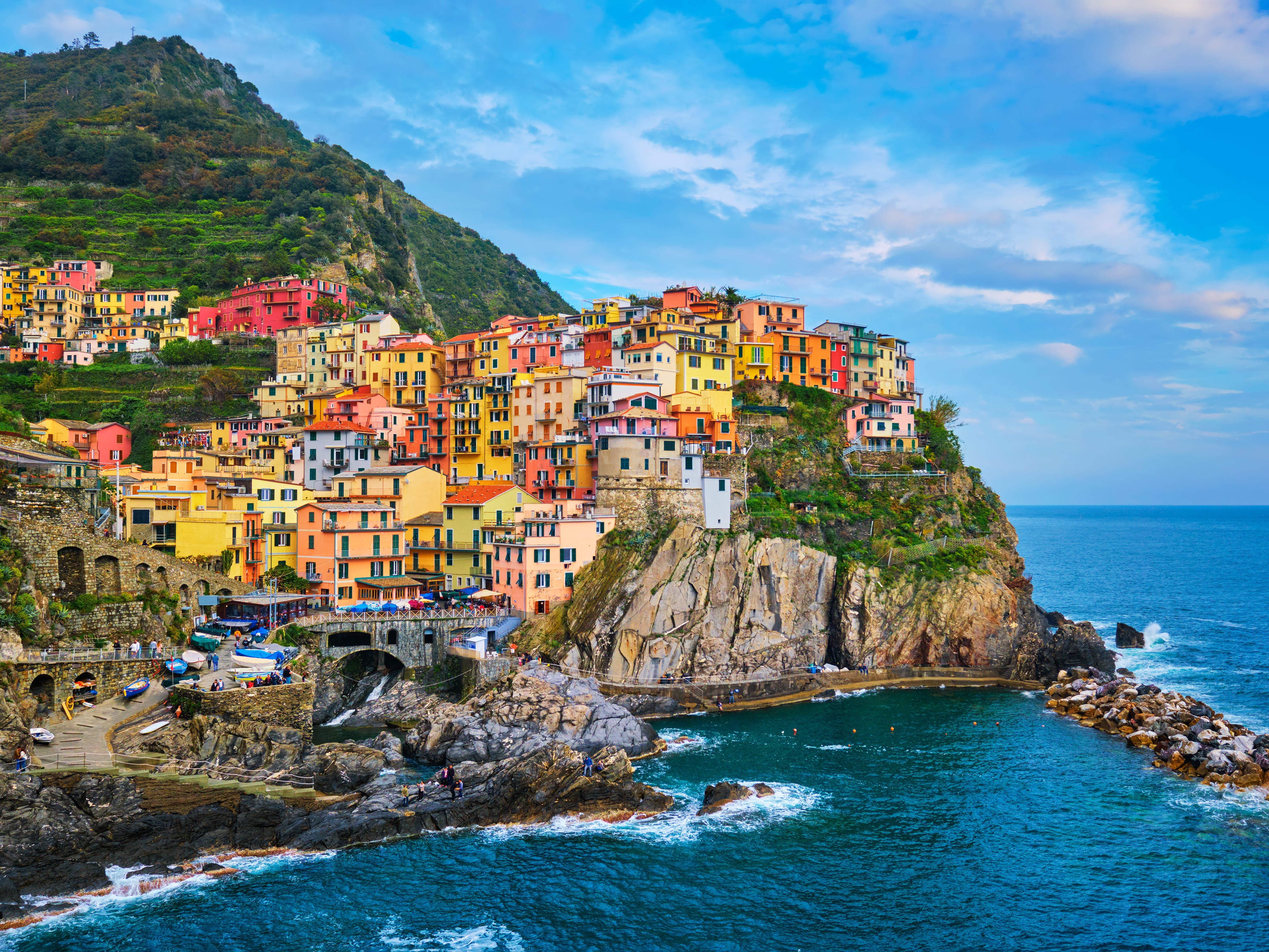 A wide shot of Manarola, one of the five towns that compose Cinque Terre. The town is composed for colorful buildings positioned on the edge of cliff with the water below.