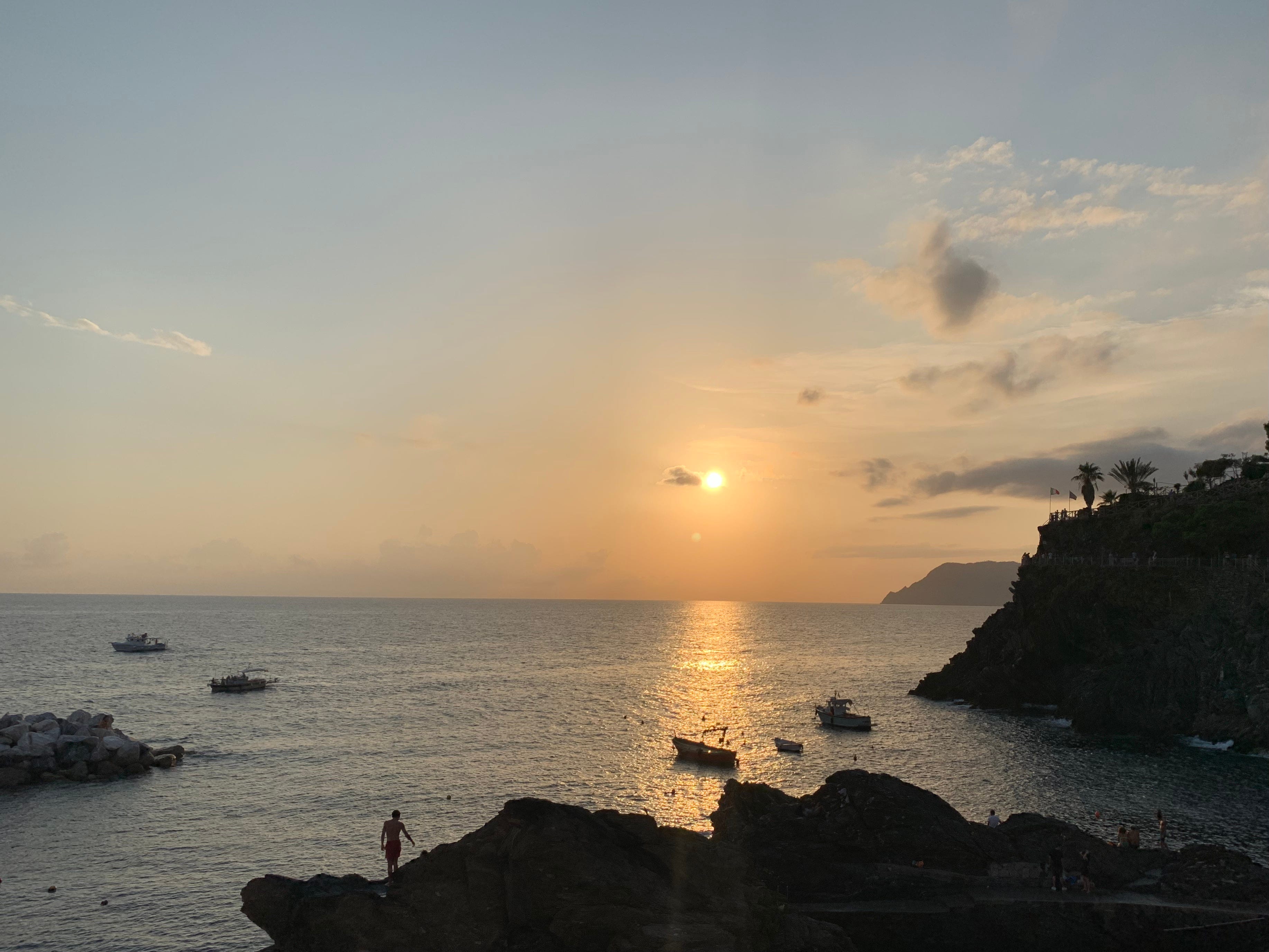 The Cilento Coast at sunset. Boats are in the water, and people are walking on the rocks.