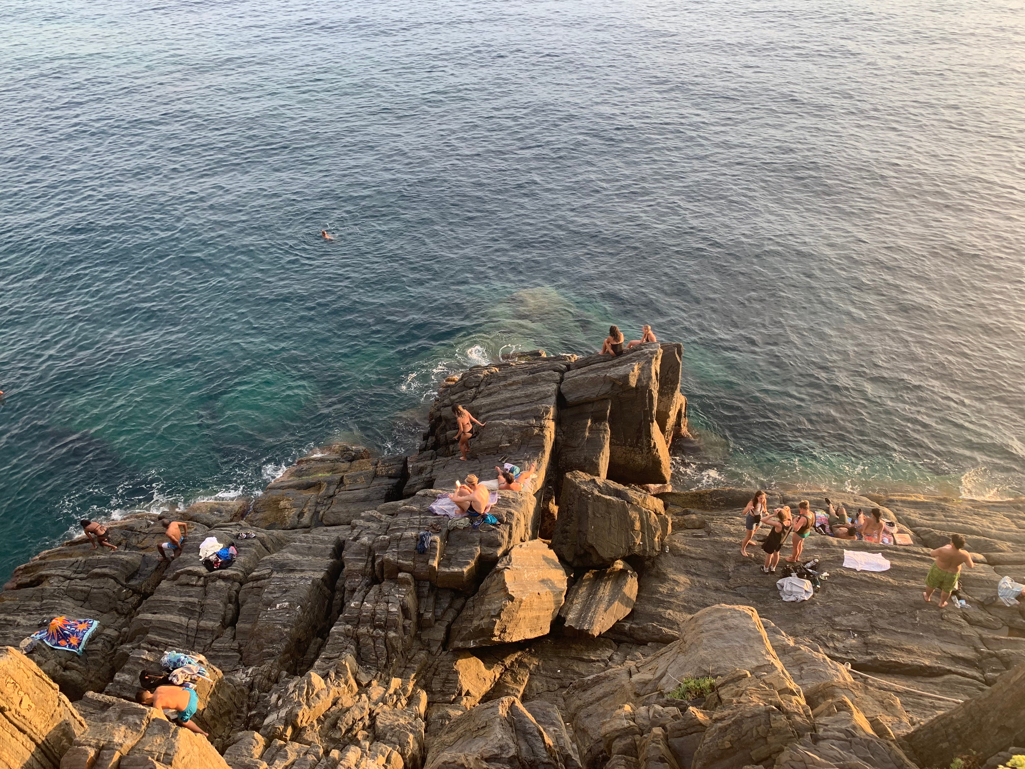 The author's view from above a large group of people relaxing on the rocks near the water in Calabria, Italy.