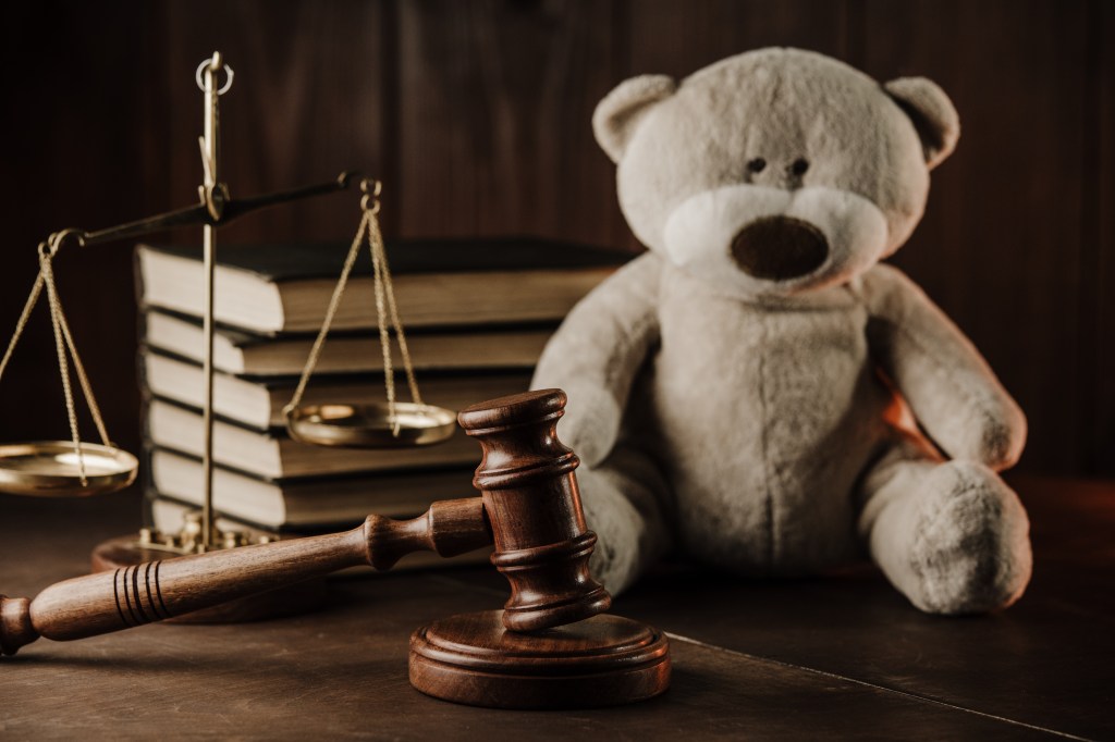 Gavel, scales of justice, and teddy bear on a desk; representing child custody in divorce proceedings.
