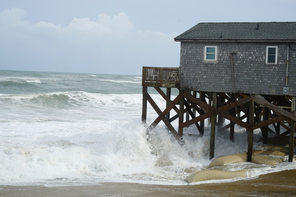 Waves crashing against a house on stilts during a hurricane.