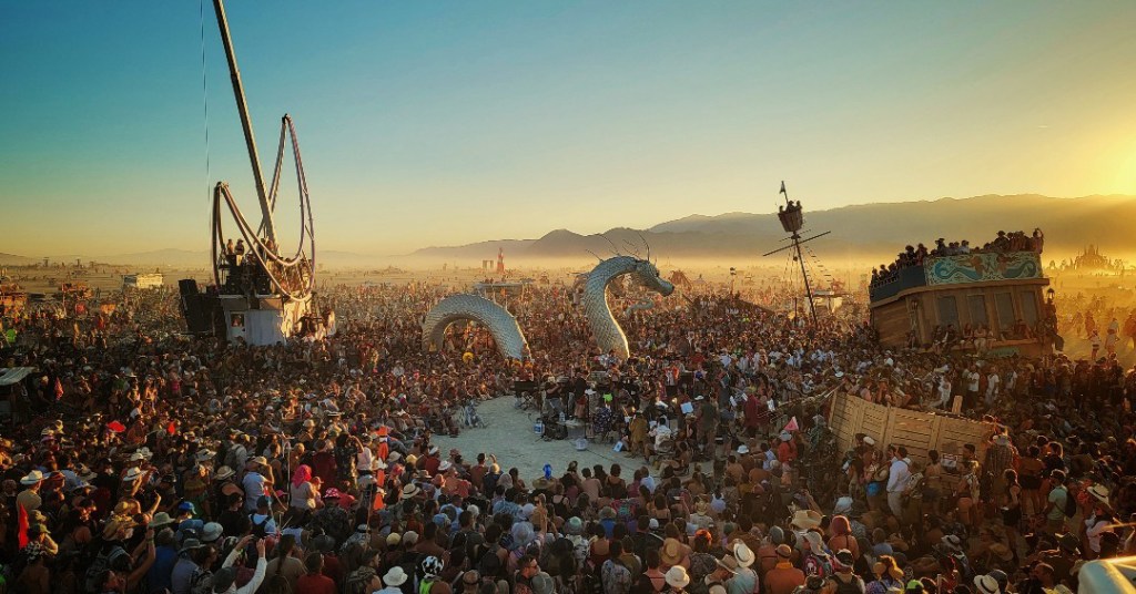 Large crowd at Burning Man festival with large art installations.