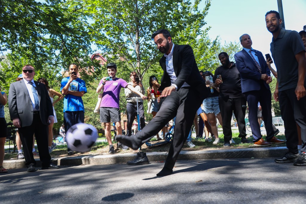 Zohran Mamdani kicking a soccer ball while campaigning in Brooklyn.