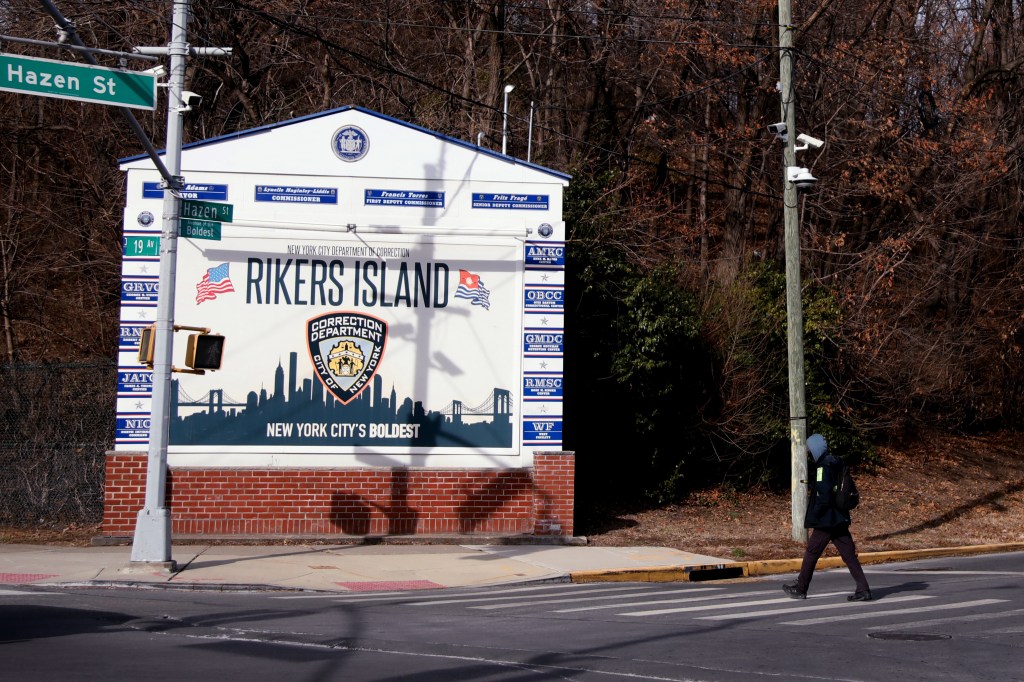 Photo of a Rikers Island sign and a person crossing the street.