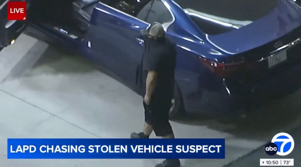 A man suspected of stealing a car, covers his face with a shirt as he fills up the stolen vehicle at a gas station during a police chase in Los Angeles on Aug. 22, 2025.