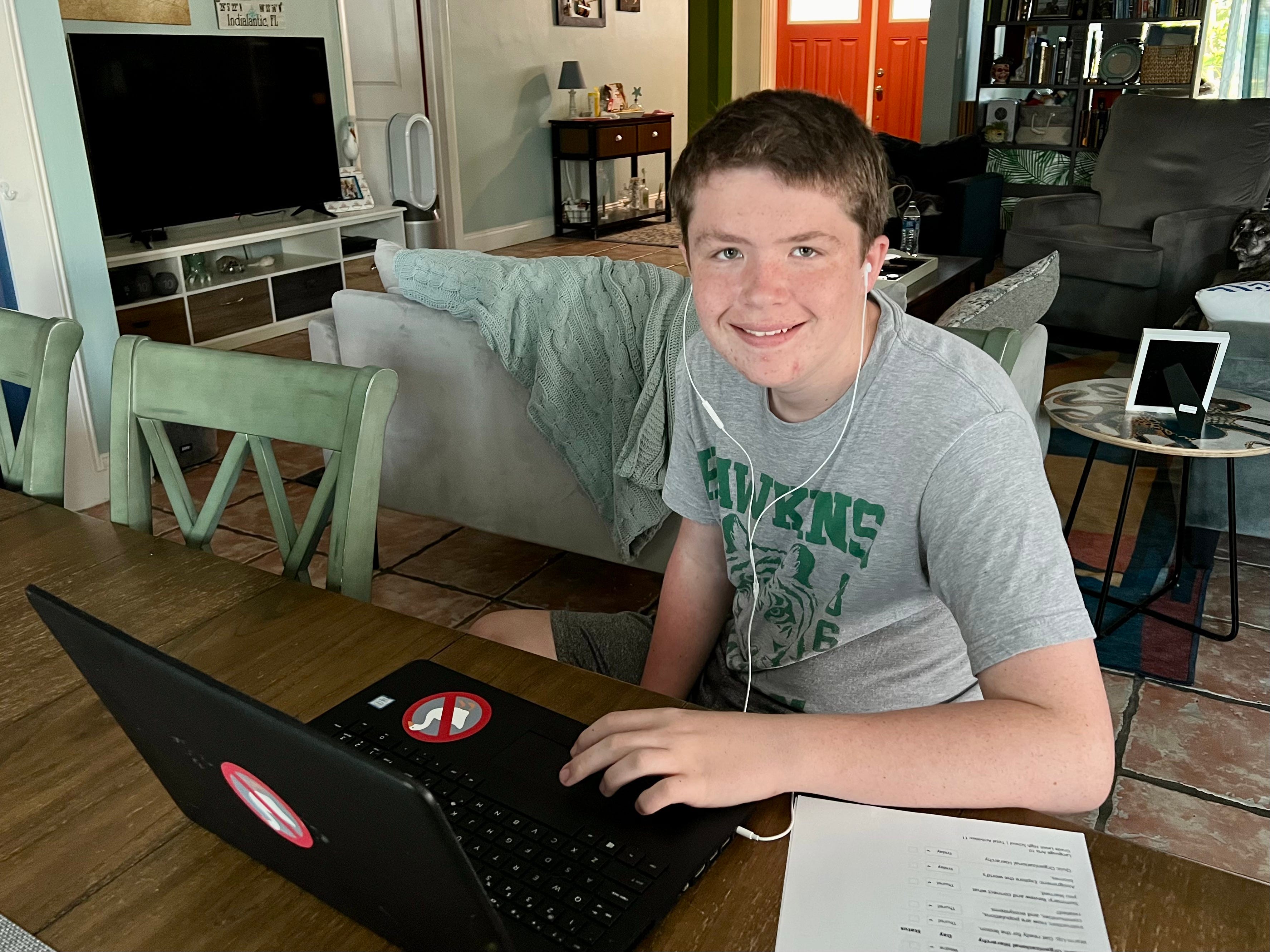 The author's son sitting at a computer with headphones in while doing homeschool.