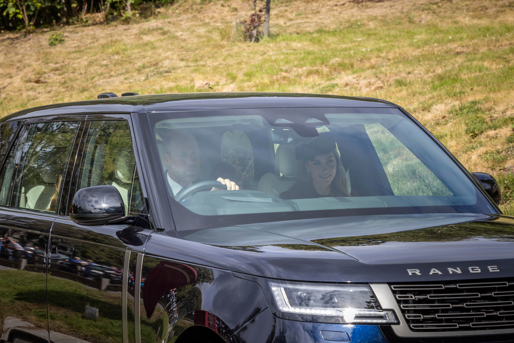 Prince William and Kate Middleton with their three kids in a car.
