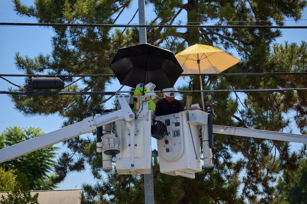 Utility workers using umbrellas for shade while repairing power lines in Los Angeles during a heatwave.