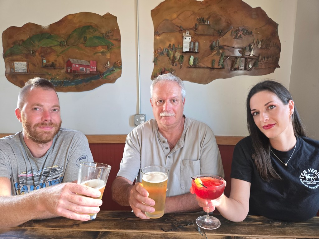 Photo of three people, Brad, Alexis, and John, raising a toast with drinks.