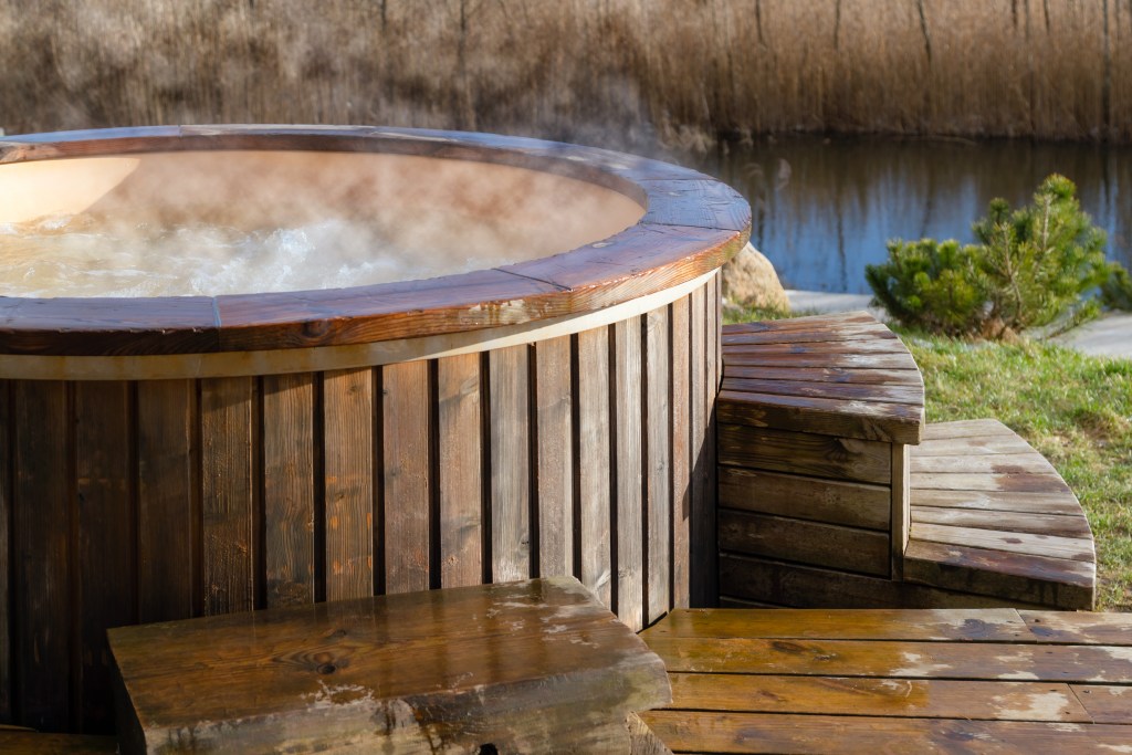 Steaming wooden hot tub outdoors near a pond.