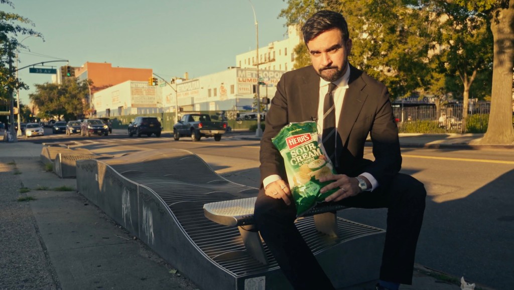 Man in suit holding a bag of chips on a city street.