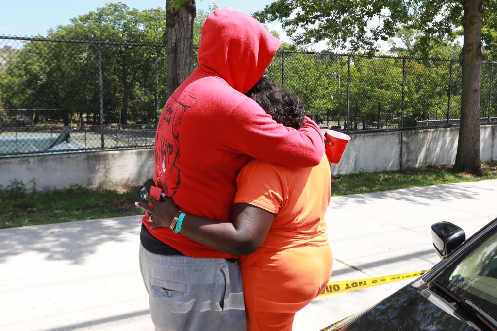 A woman in orange hugs a person in red near police tape at a park.